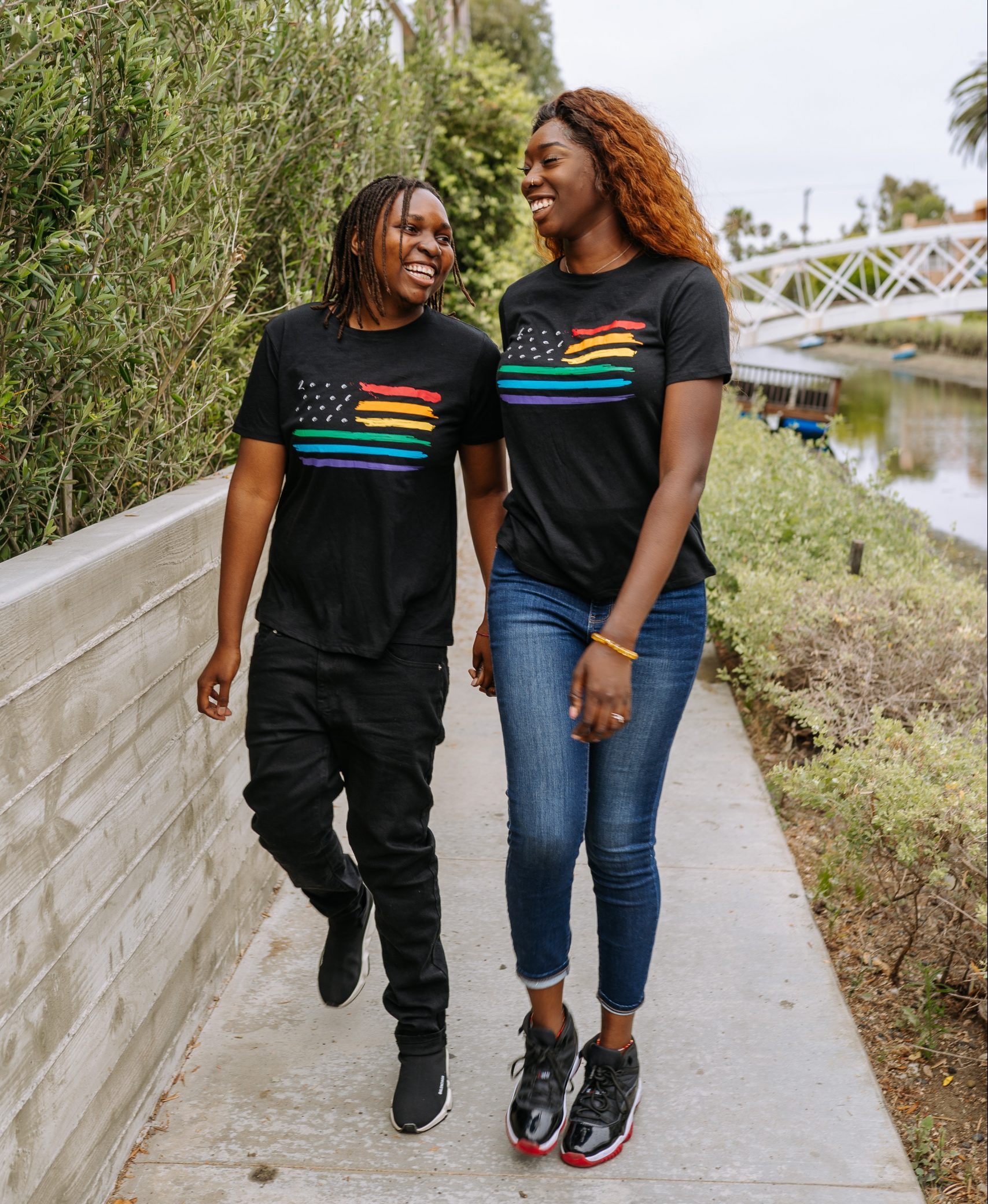 Two queer women of color wearing pride shirts walking on the street