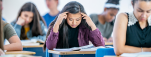 young person with hands in head leaning over desk at school